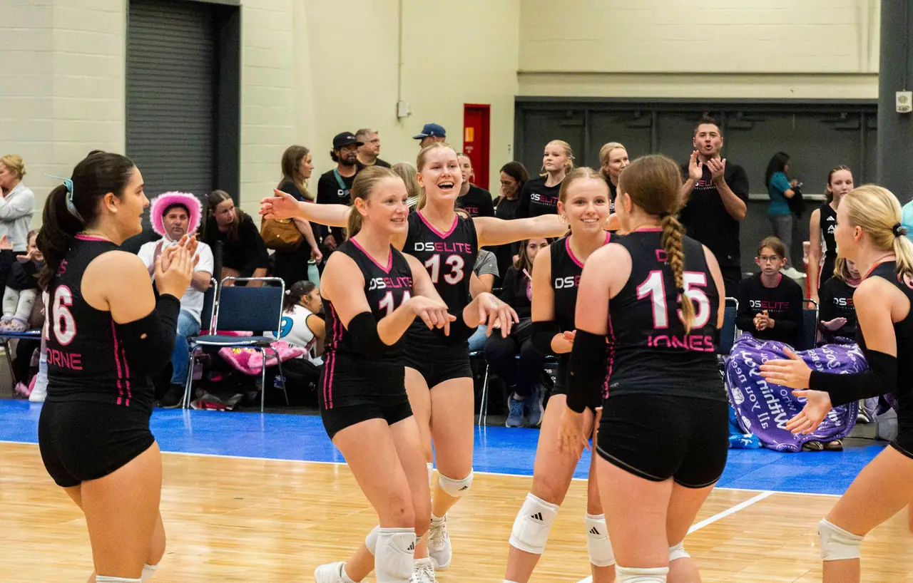 DS Elite players in black uniforms running together to celebrate a point while families cheer on the sideline