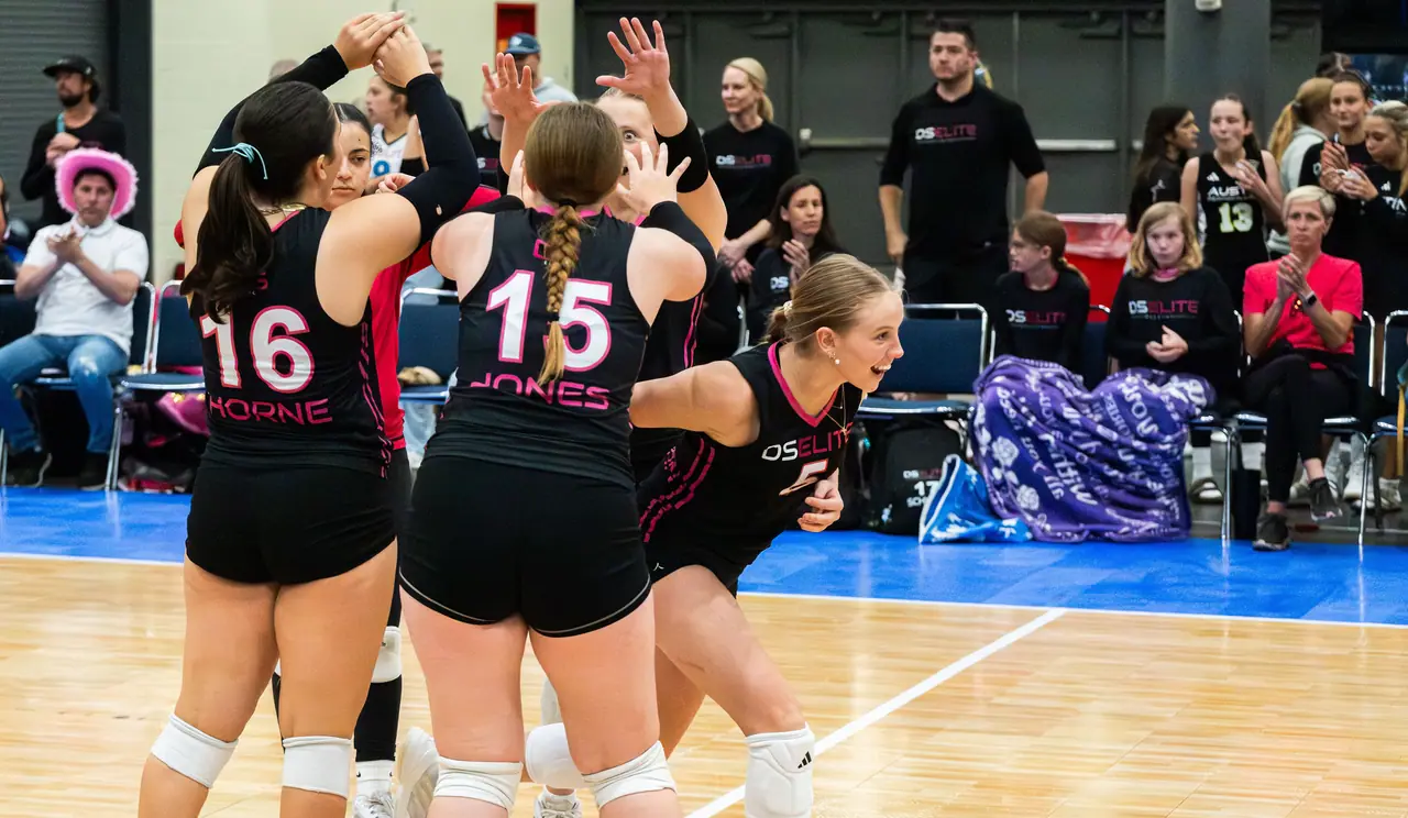 DS Elite players in black uniforms leaping into a group high five as their bench and parents cheer