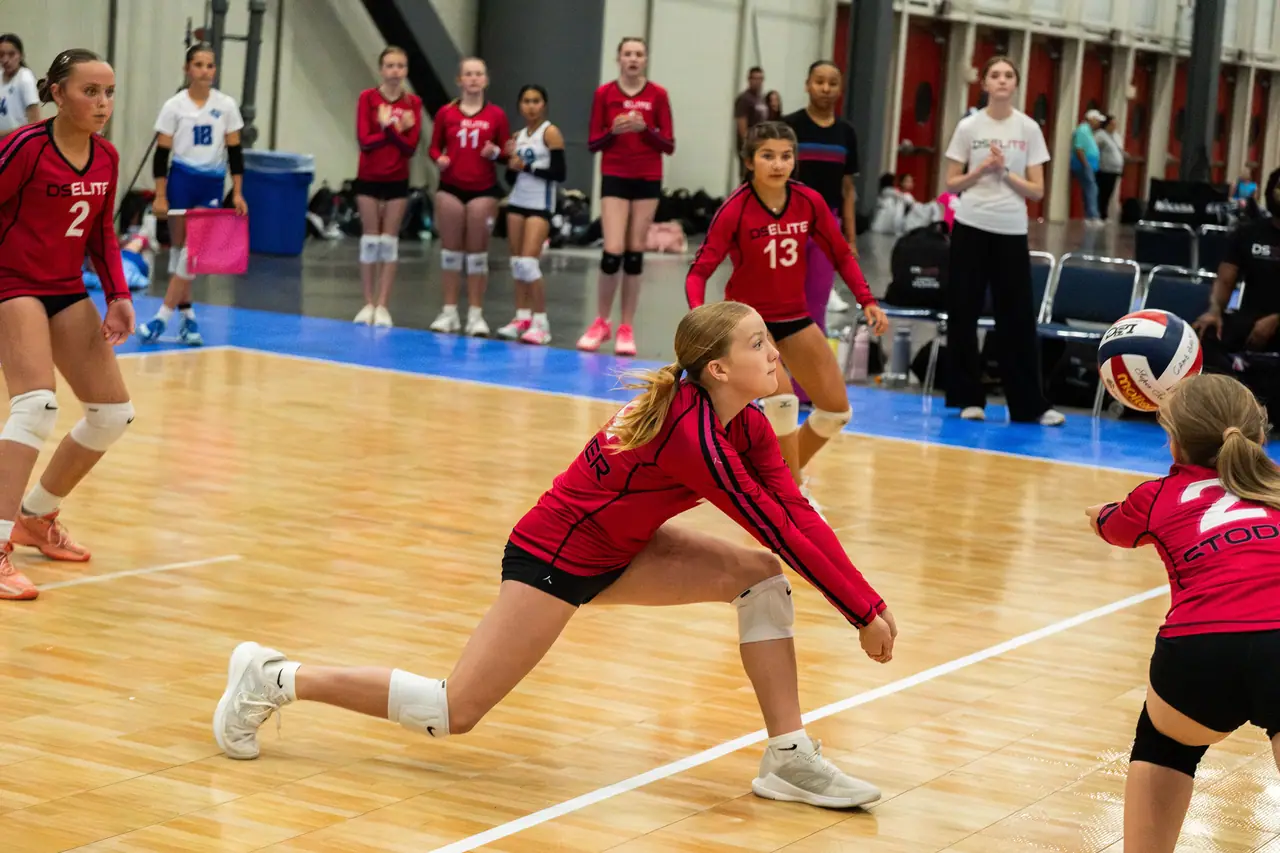 DS Elite defender in a red uniform in a deep lunge, passing a hard-driven ball