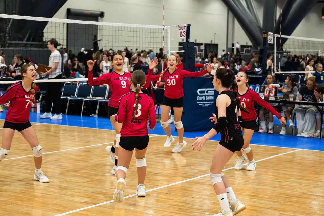 DS Elite teammates in raspberry uniforms rushing together, arms up and laughing, after winning a point