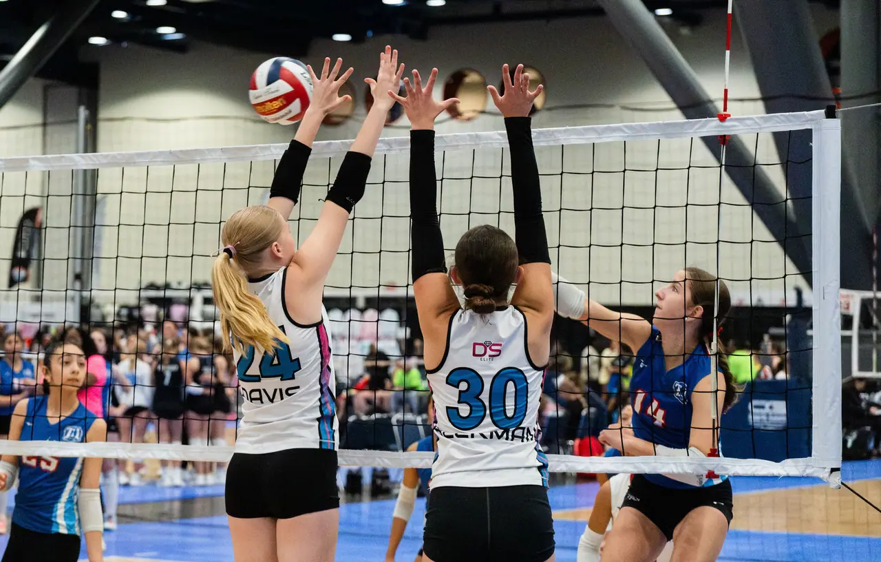 Two DS Elite blockers in white uniforms up at the net with their hands spread over the tape