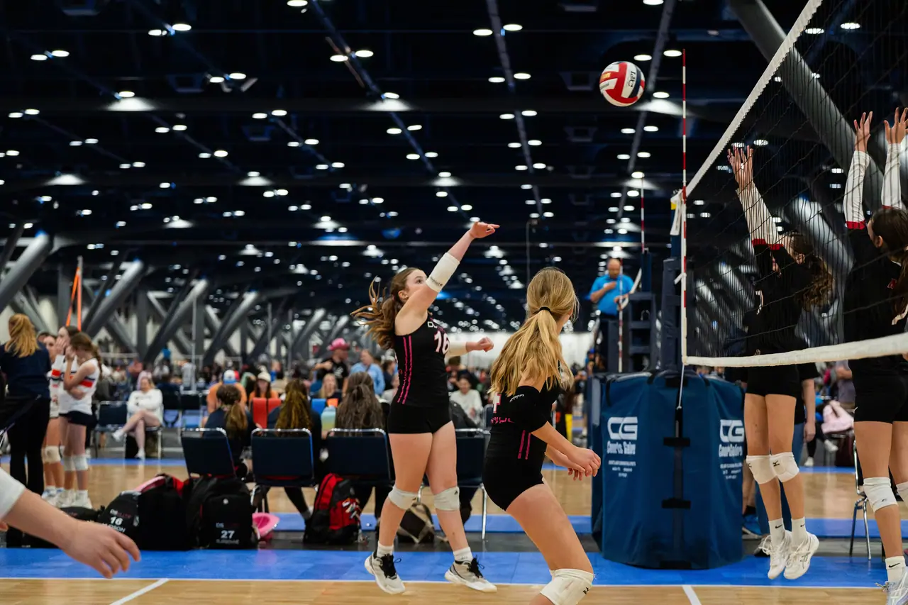 DS Elite hitter in a black uniform in the air, following through on an attack toward two blockers