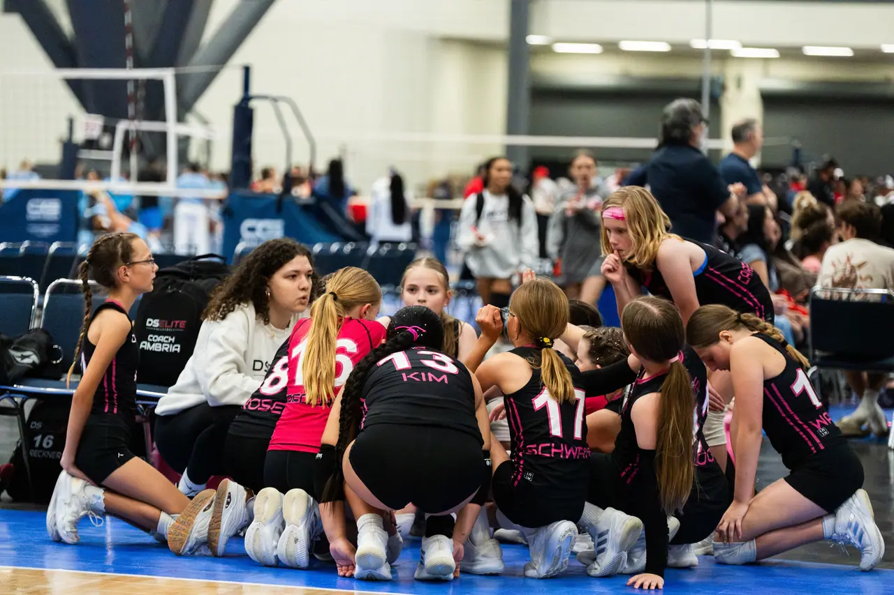 Younger DS Elite team kneeling in a tight circle on the court for a team talk with a staff member